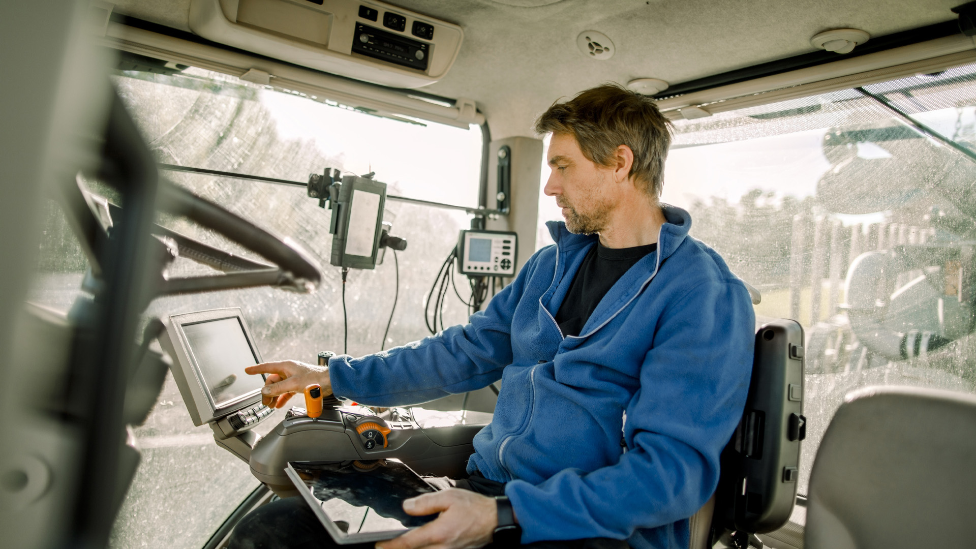 Man sitting in farm equipment operating touchscreen while holding another tablet device